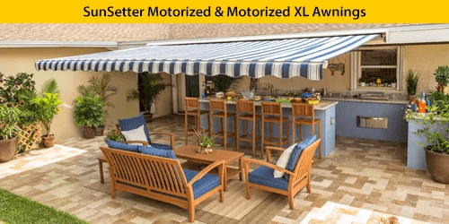 A blue-and-white striped motorized awning extends over a patio with outdoor seating and a dining area, providing shade next to an outdoor kitchen in a backyard setting.
