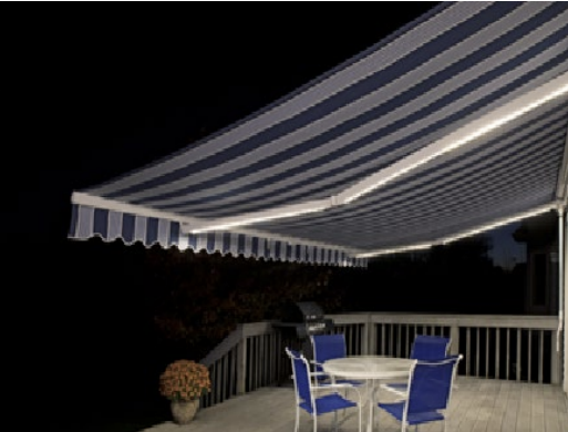 A backyard deck at night features a round table with four blue chairs, flower pot, and a blue-and-white striped retractable awning with built-in lights. A grill is visible in the background.